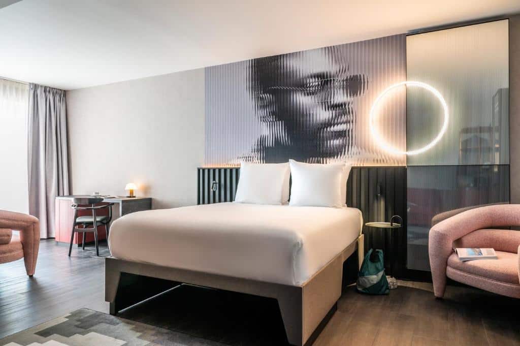 Quarto do Tribe Amsterdam, de 32 m², com cama de casal, um cadeirão e uma mesinha com cadeira, e um quadro por cima da cama