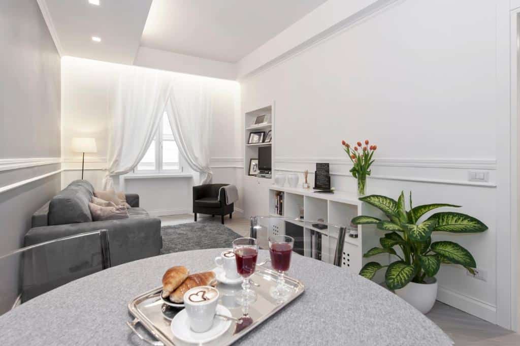 sala do Trevi Apartment, com mesa redonda e cadeiras com o pequeno-almoço posto, sofá-cama, janela grande com cortinas claras, nichos decorativos em frente e uma poltrona