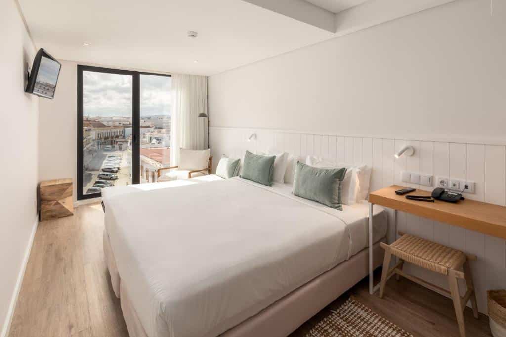 Um quarto moderno no Pure Formosa Concept Hotel em Olhão, com uma cama grande, secretária, TV de ecrã plano, cadeira e janela com vista para a cidade.