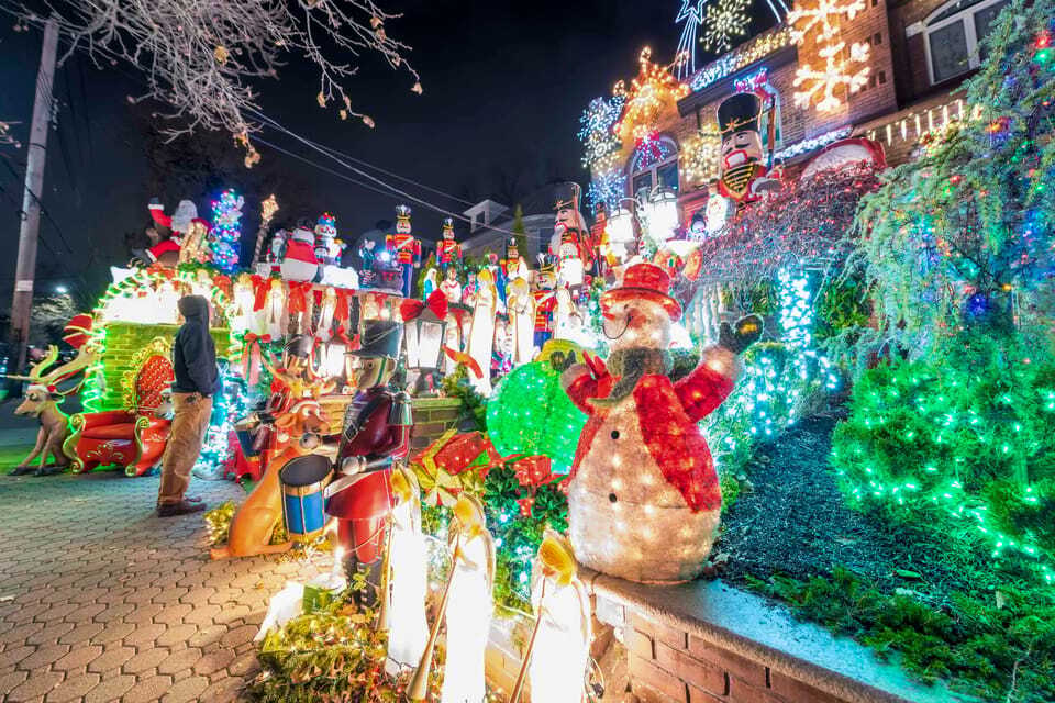 Decoração de Natal ao ar livre muito elaborada durante a noite, com figuras iluminadas e uma casa coberta de luzes.