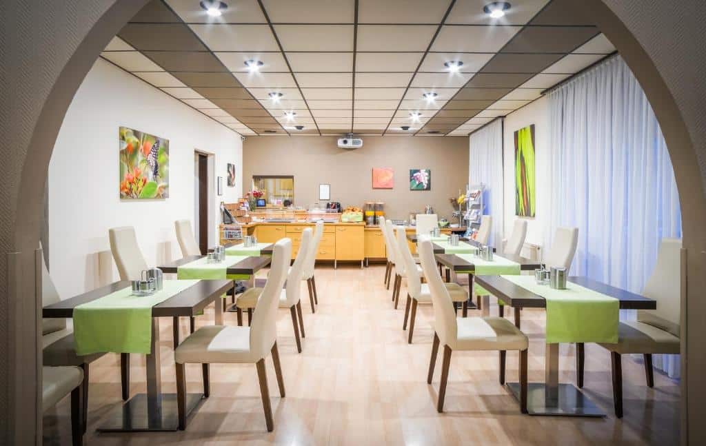Sala de refeições moderna no Hotel-Pension Wild, com oito mesas, cadeiras brancas, toalhas verdes e um buffet ao fundo.