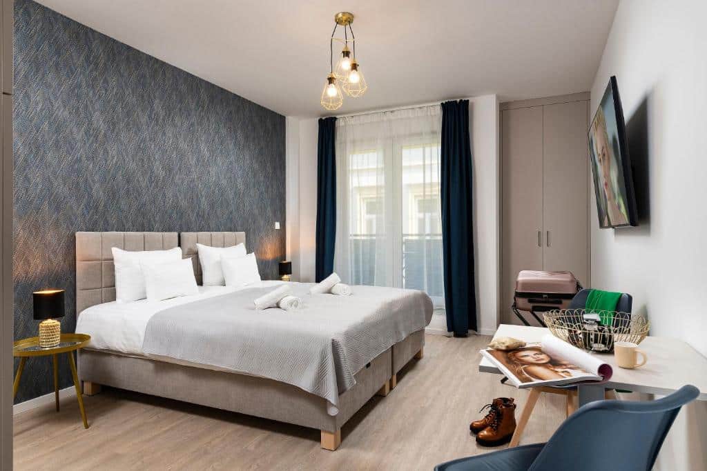 Quarto do Bo18 Hotel Superior com uma cama de casal, parede com apontamentos em azul, TV, pequena secretária, mala e janela com cortinas.