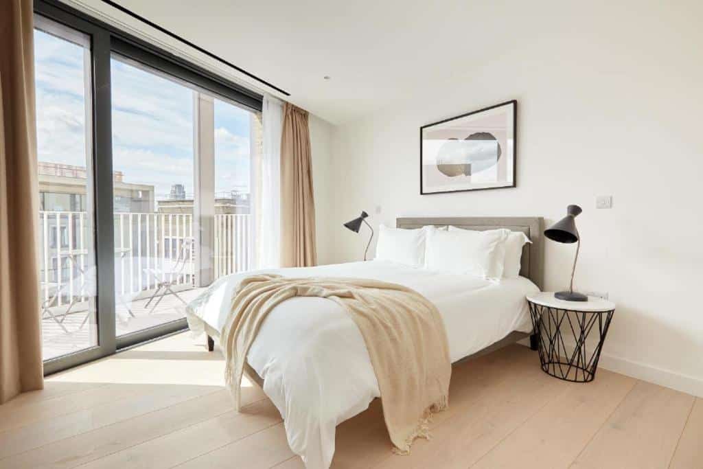Quarto do Southwark by Q Apartments com uma varanda com cadeiras, cama de casal, duas cabeceiras orgânicas com candeeiros, um quadro e chão de madeira.