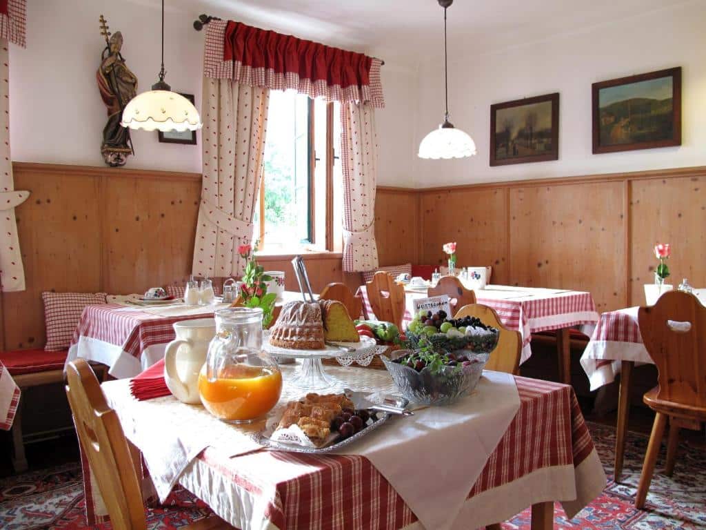 Sala de refeições acolhedora no Hotel Schneider-Gössl, com paredes de madeira, toalhas axadrezadas vermelhas e mesas com comida e bebida para o pequeno-almoço.