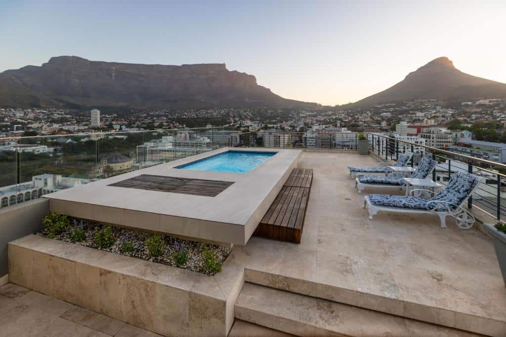 Piscina na cobertura do Pepperclub Hotel com espreguiçadeiras e vista para a cidade e as montanhas ao pôr do sol.