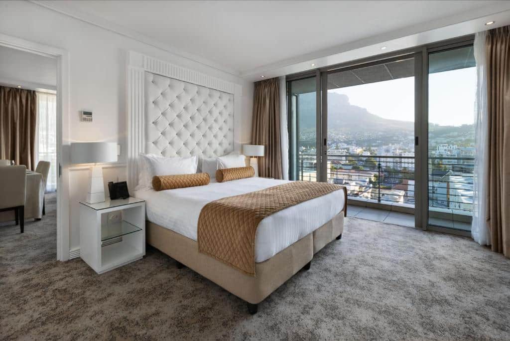 Quarto do Pepperclub Hotel com cama grande, detalhes dourados, portas de vidro para uma varanda e vista da cidade com montanhas ao longe.