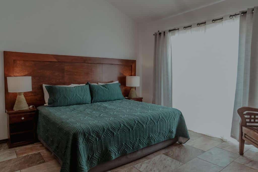 Quarto de casal no Fabiola Condo Hotel com cama de madeira e roupa de cama verde junto a uma janela.