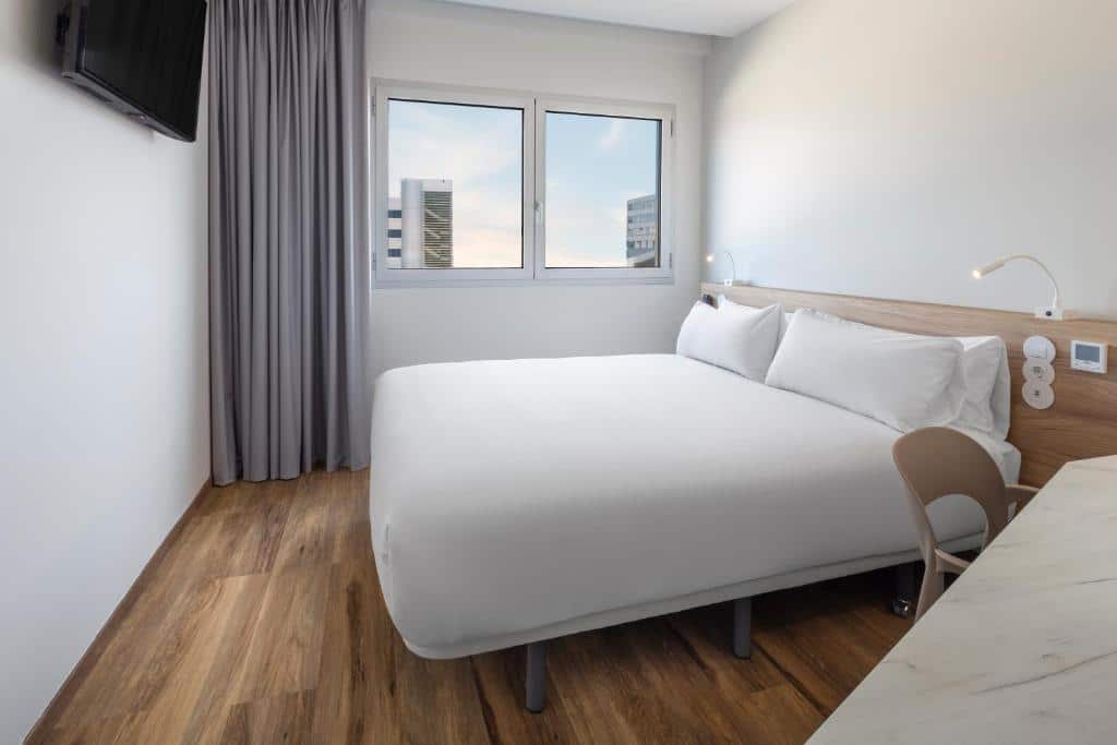 Quarto do B&B HOTEL Lisboa Aeroporto, com uma janela do lado esquerdo e uma televisão na parede em frente à cama.