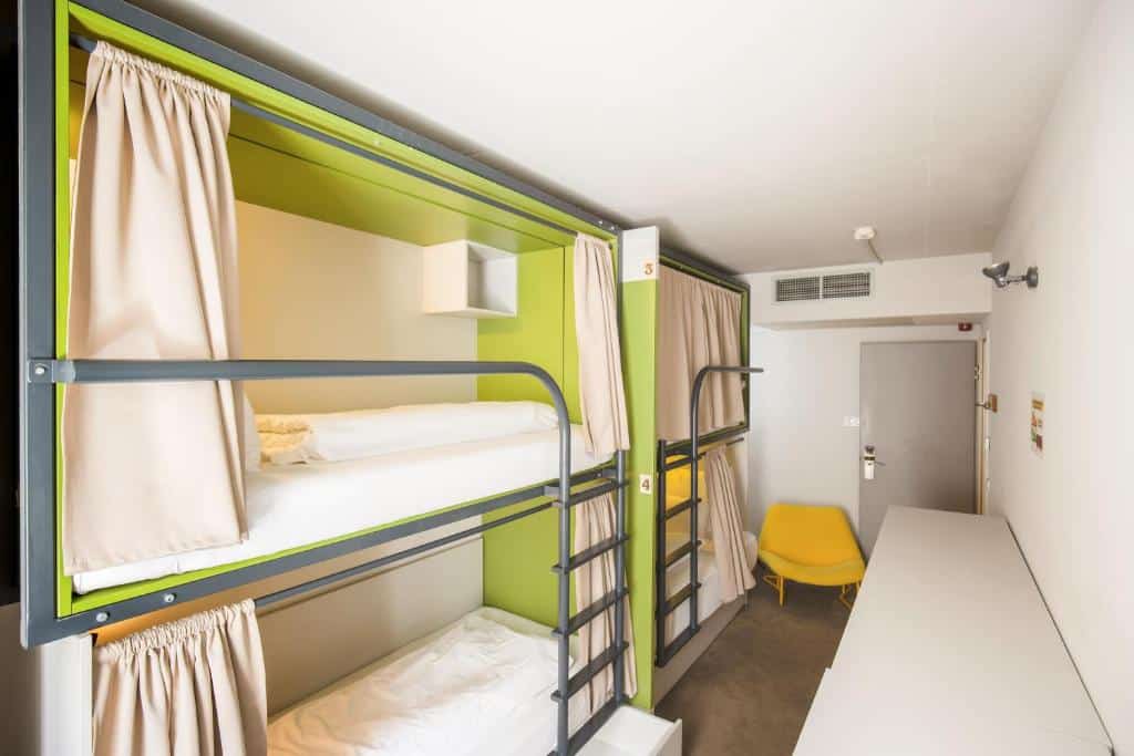 Um quarto do Maverick Central Market com dois beliches com cortinas, uma cadeira amarela, uma secretária branca e uma porta ao fundo.