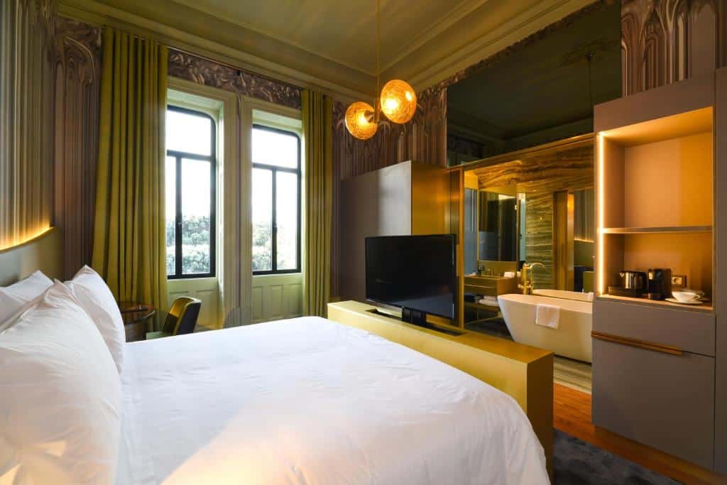 Quarto do Vila Foz Hotel & SPA com cama de casal, televisão em frente e casa de banho com banheira ao fundo.