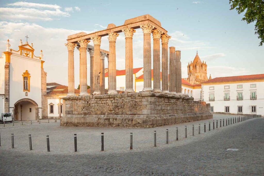 Templo Romano de Évora com colunas de mármore e igreja ao fundo em Portugal. Ilustra este artigo sobre o que fazer em Évora.