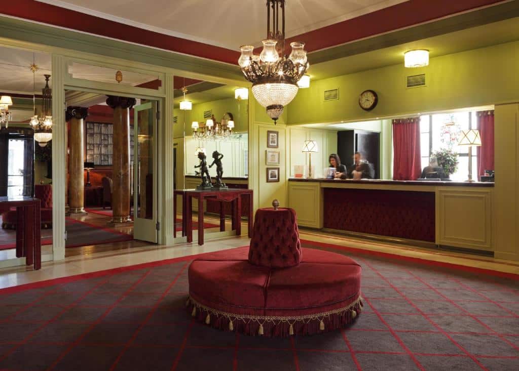 Átrio do Grande Hotel do Porto com poltrona redonda de veludo vermelho, paredes verdes, lustres e receção.