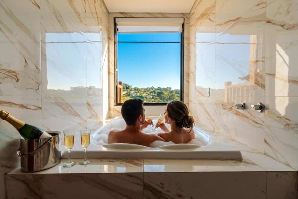 Casal relaxando em banheira de hidromassagem com champanhe e vista para área verde