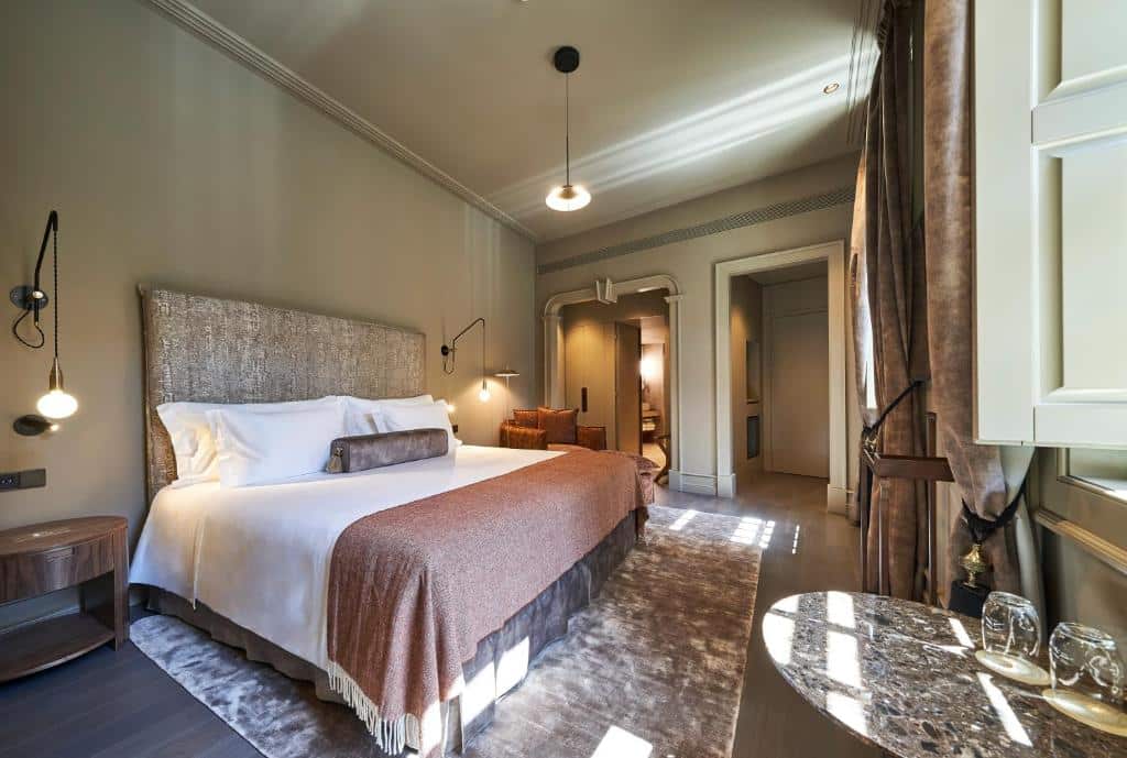 Quarto do PortoBay Flores com cama de casal ampla e uma poltrona castanha ao lado.