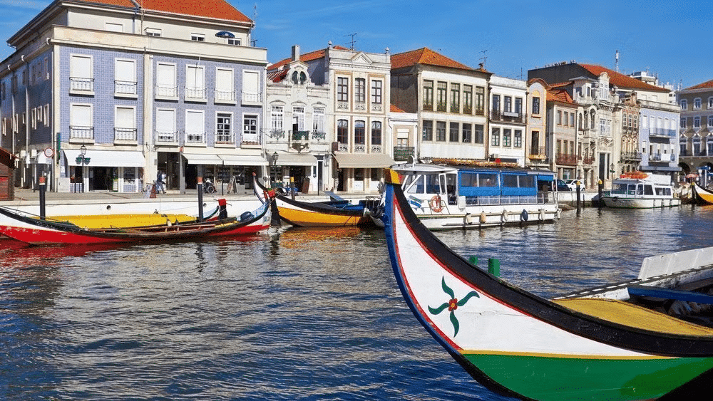 Barco moliceiro num canal de Aveiro, com mais barcos ao fundo e casas coloridas.