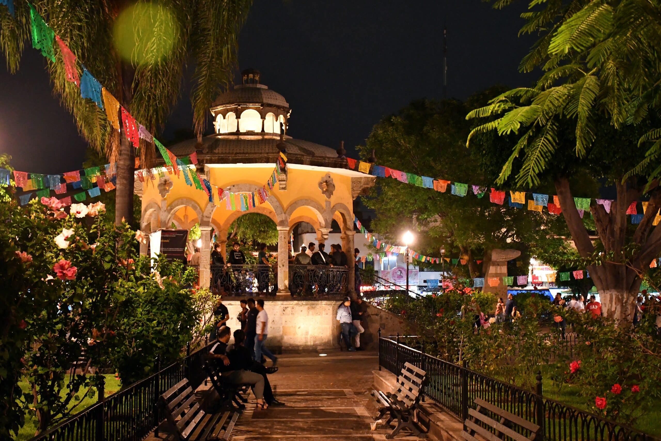 Jardim Hidalgo com coreto iluminado e decoração festiva à noite, em zona ajardinada com palmeiras, em Tlaquepaque.