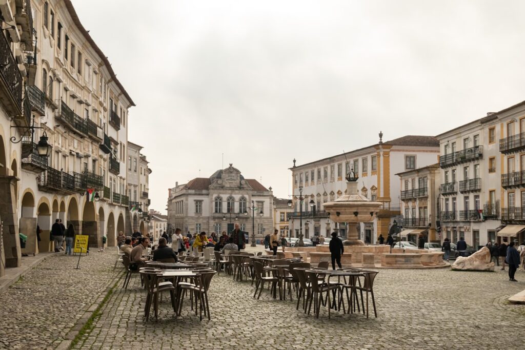 Praça histórica com chafariz, mesas e cadeiras, edifícios antigos com arquitetura portuguesa