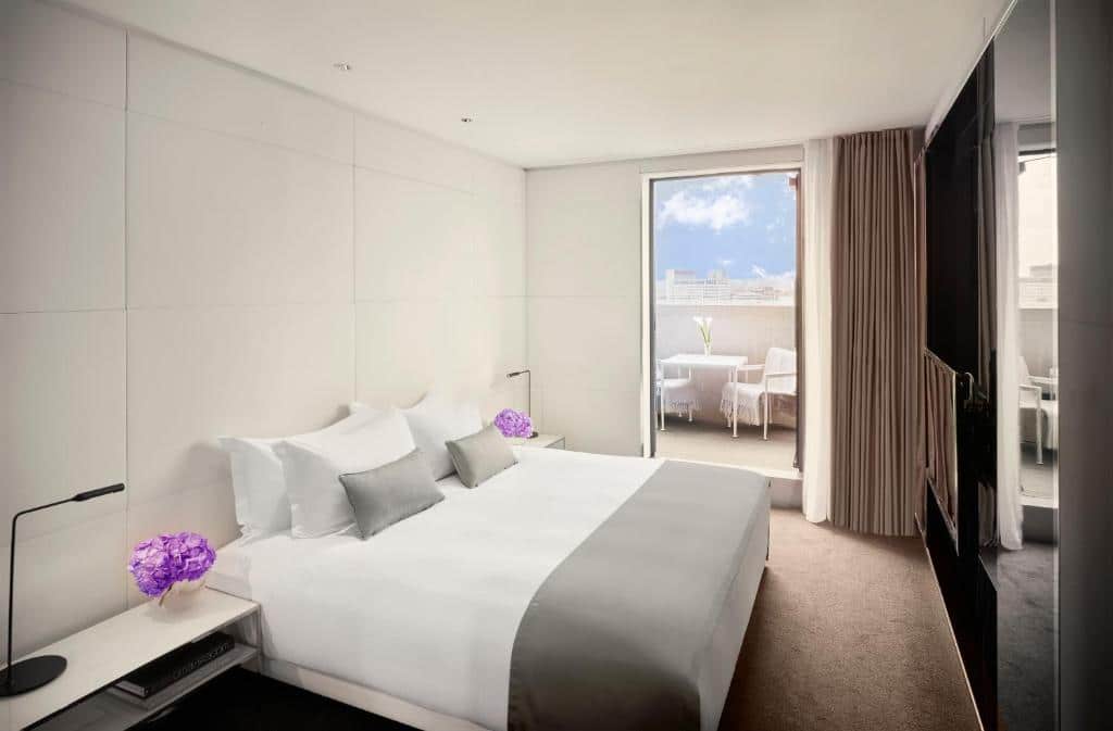 Quarto do ME London by Melia com cama de casal, varanda com mesa e duas cadeiras, televisão e chão em alcatifa