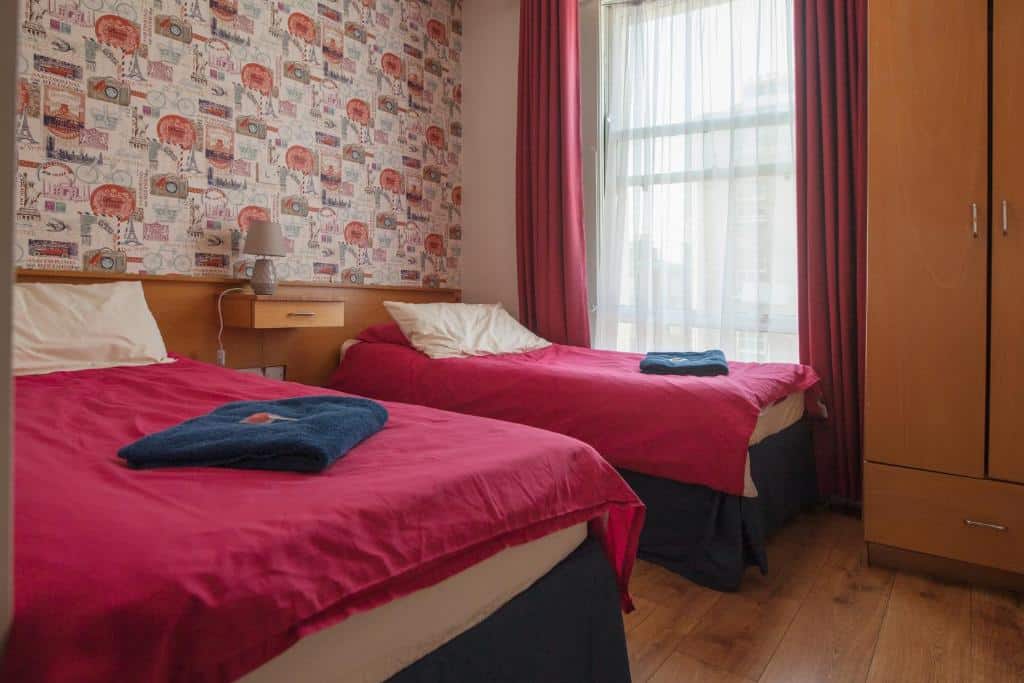 Quarto no Ashfield Hostel, com camas de casal vermelhas e armário de madeira.