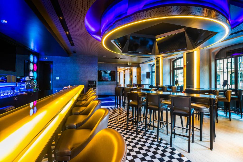 Sala e bar do Pestana CR7 Lisboa com decoração moderna e luzes roxas e amarelas, um balcão de bar com cadeiras estofadas, televisões nas paredes e mesas compridas com cadeiras