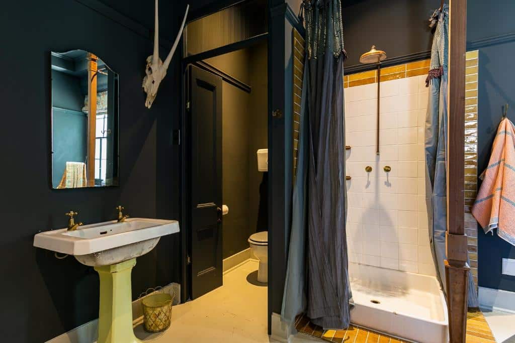 Casa de banho no Hotel Lola com lavatório de pé, espelho de parede, chuveiro com cortina, toalha e sanita numa alcova separada.