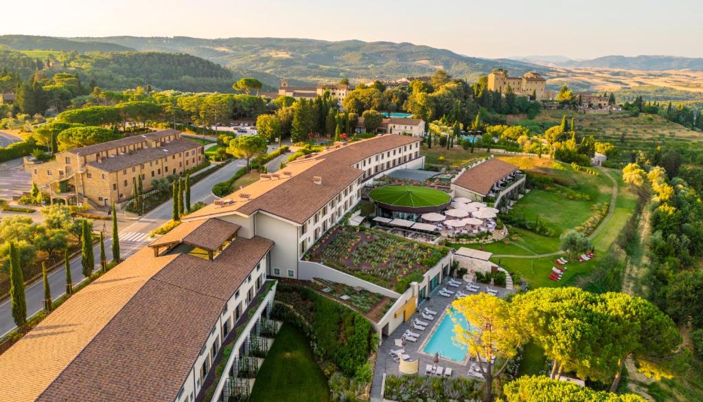 Vista aérea do Toscana Resort Castelfalfi, um dos hotéis na Toscana, com um edifício grande de várias janelas, plantações à frente, jardim e muito verde em redor