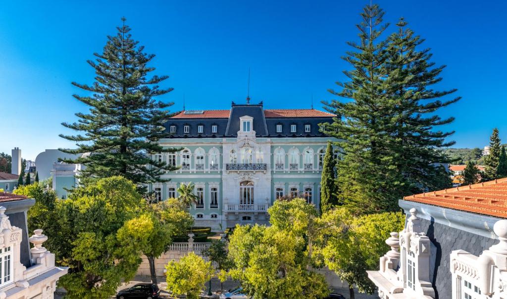 Edifício do Pestana Palace Lisboa Hotel & National Monument, um palácio de época em tons de branco e verde-claro rodeado de árvores