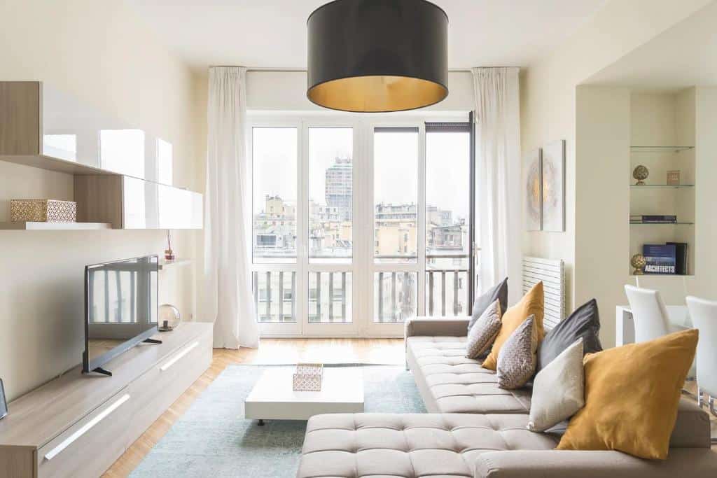 Sala de estar do Heart Milan Apartments San Sepolcro Duomo com um sofá com várias almofadas, uma varanda com cortinas, um móvel com uma televisão e um lustre redondo preto