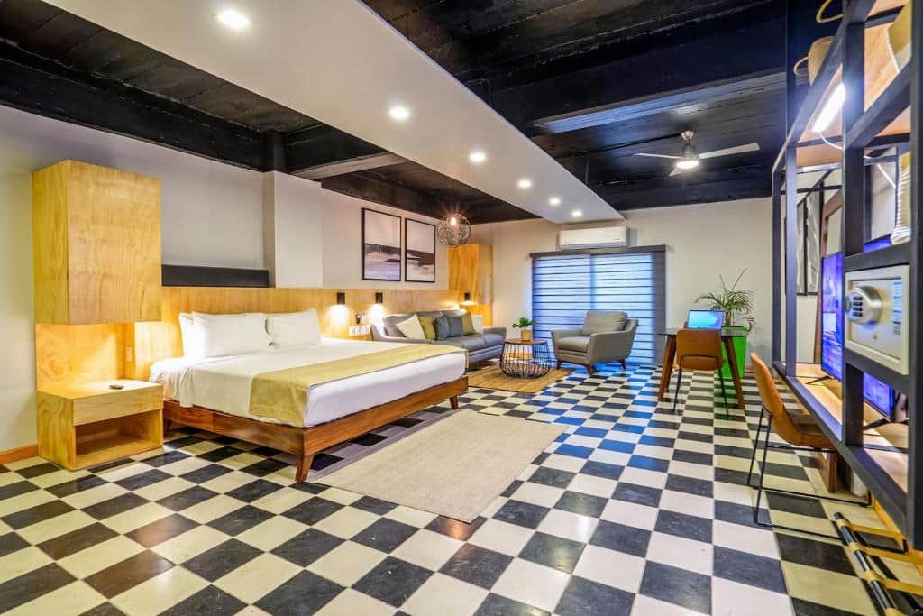Quarto espaçoso do Joint Boutique Hotel com uma cama king-size, pavimento xadrez, zona de estar, secretária, TV e decoração moderna sob vigas escuras.