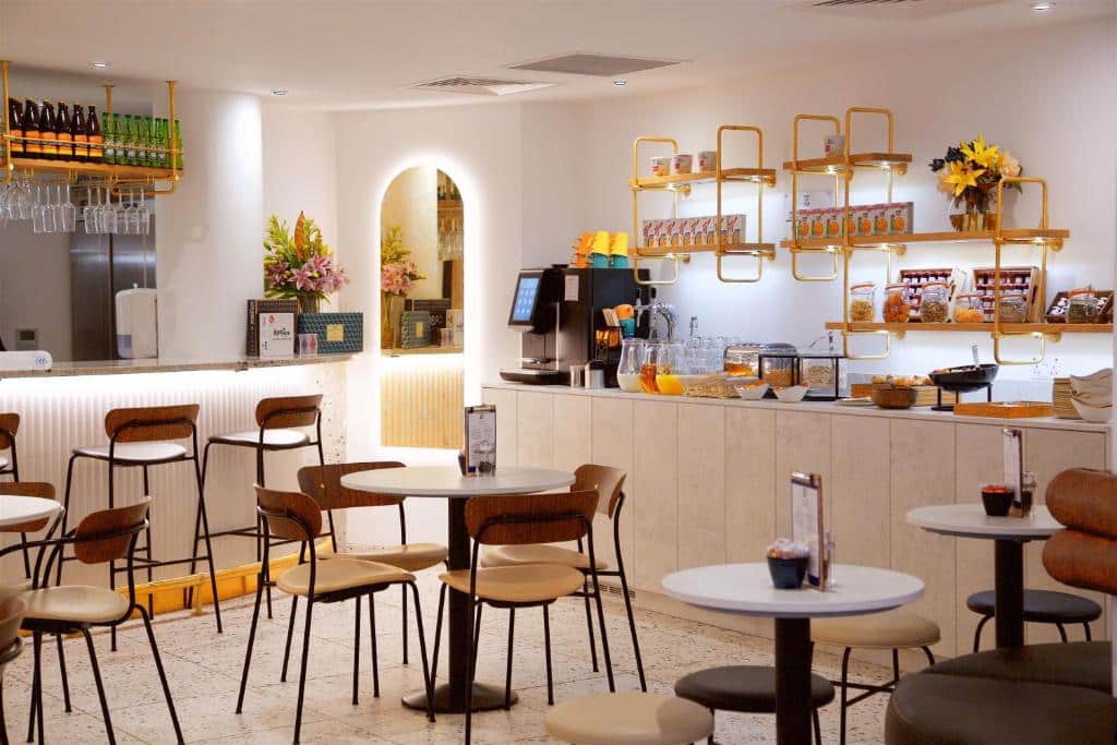 Área de refeições do The Z Hotel Trafalgar com mesas redondas, cadeiras de madeira e um balcão de bar