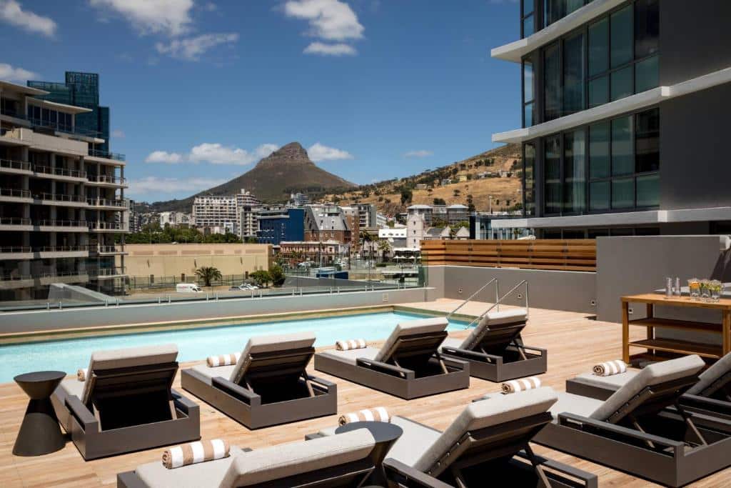 Deck da piscina exterior no AC Hotel by Marriott com espreguiçadeiras, edifícios da cidade e uma montanha ao fundo.