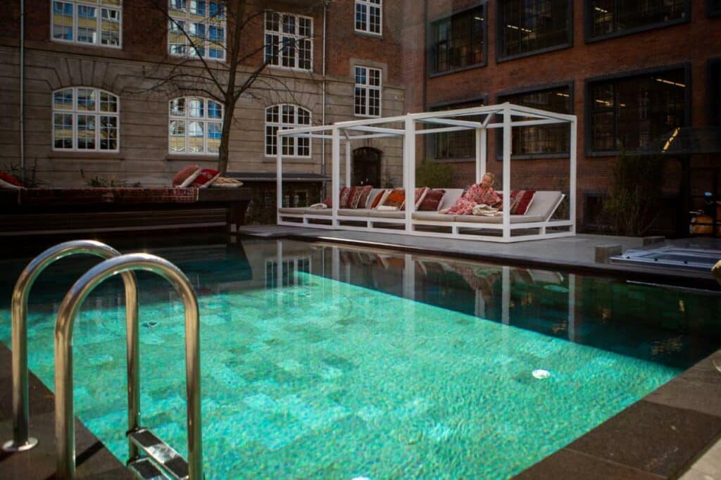 Piscina do hotel Bryggen Guldsmeden, com várias espreguiçadeiras e uma pessoa sentada numa delas. Em redor vê-se o hotel.