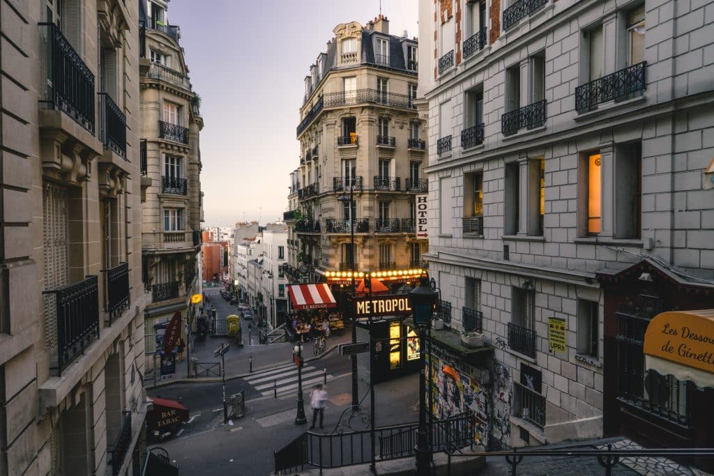 Rua de Montmartre, em Paris, com edifícios antigos, uma entrada de metro e pessoas a passear junto a lojas e cafés ao final do dia.