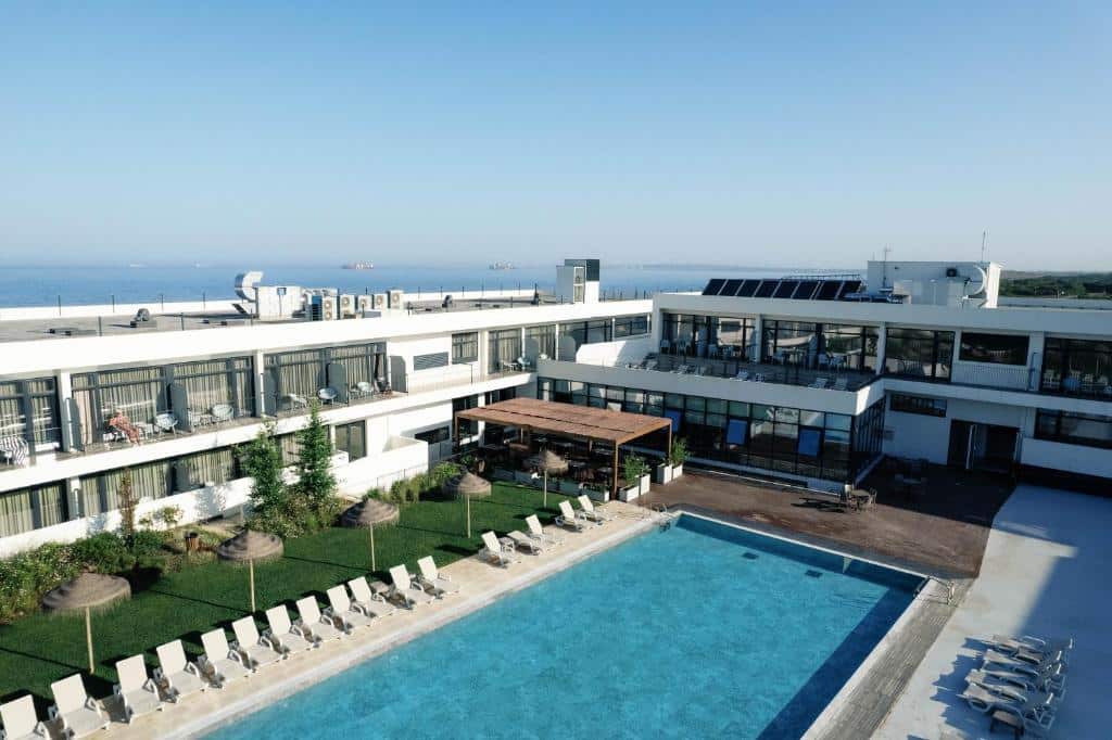 Piscina retangular azul com espreguiçadeiras e vista para o mar no Porto Covo Praia Hotel & SPA