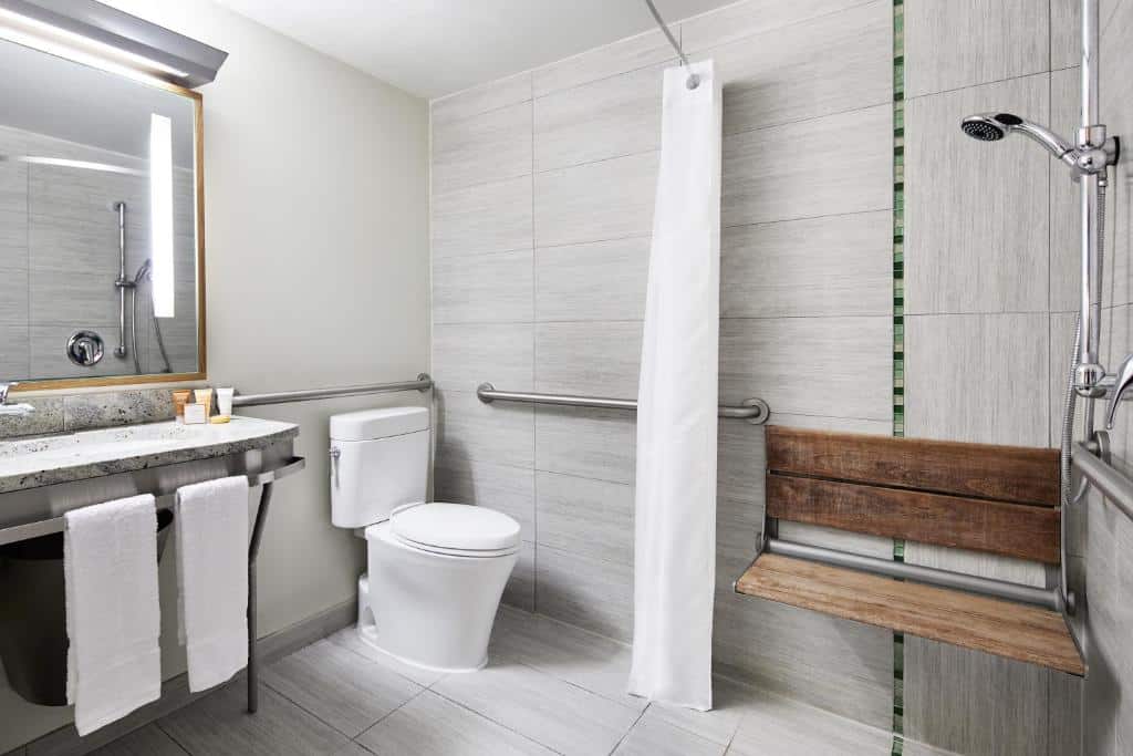 Casa de banho do The Jewel Hotel com lavatório em bancada de mármore à esquerda e um espelho com luz embutida. À direita, a sanita e, ao fundo, uma cabine de duche com parede de vidro.