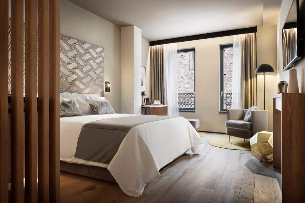 Quarto do Speronari Suites com duas janelas com cortinas, pavimento que imita madeira, cama de casal, mesinha com cafeteira e chávenas, poltrona e candeeiro de pé