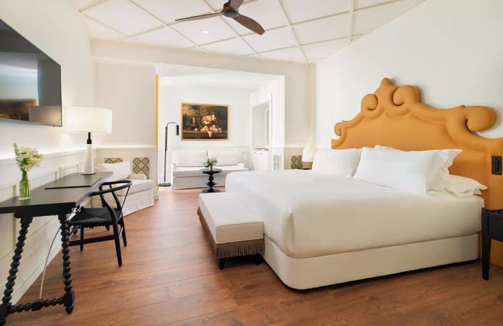 Quarto espaçoso do H10 Casa de la Plata com cama de casal de cabeceira amarela, secretária, televisão e um sofá ao fundo.