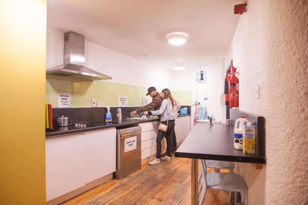 Casal jovem a preparar uma refeição numa cozinha do Ashfield Hostel, com soalho de madeira e eletrodomésticos modernos.