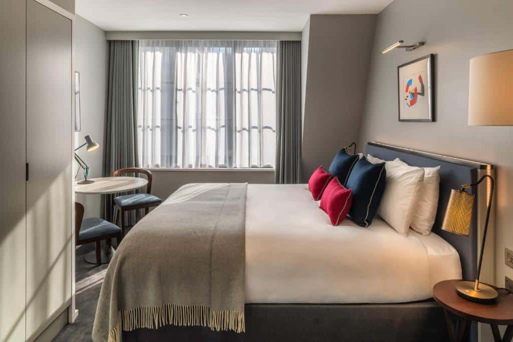 Quarto do The Resident Covent Garden com janela com cortinas, cama de casal, mesa com duas cadeiras e um armário