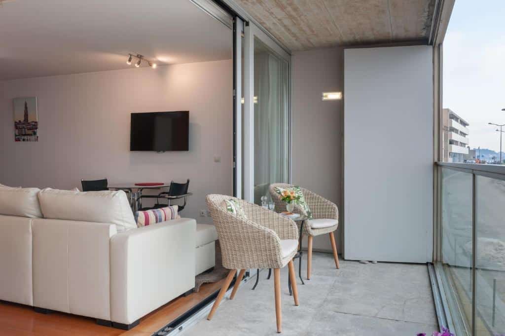 Varanda do Bartolomeu Beach Apartments, com duas poltronas e, ao fundo, uma sala de estar com sofá e TV.