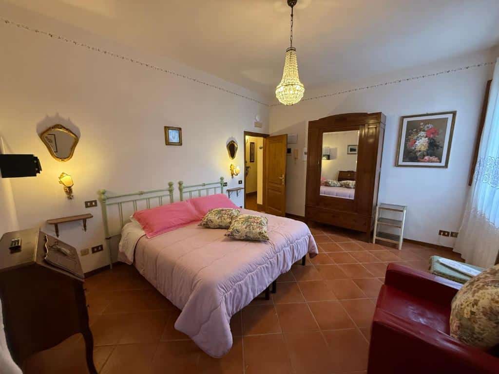 Quarto de casal com cama de ferro e roupa de cama rosa, cómoda antiga e espelho com moldura de madeira