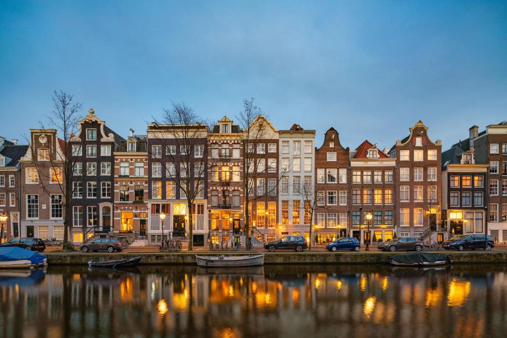 Edifícios estreitos e históricos do Ambassade Hotel ao início da noite, refletidos na água do canal em frente