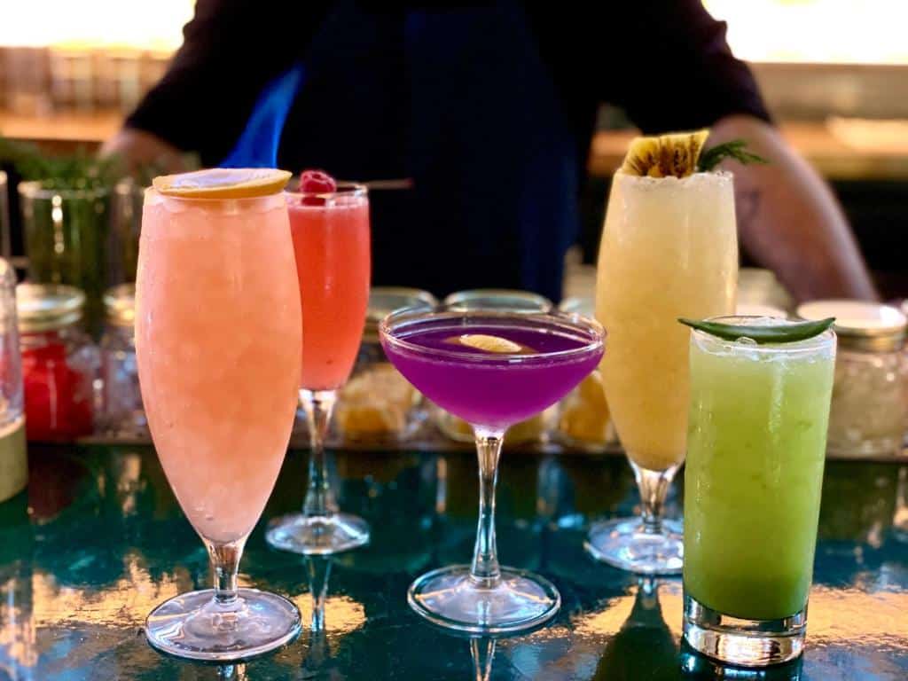 Cinco bebidas coloridas no bar do Pod Times Square; atrás do balcão vê-se um homem com os braços apoiados na mesa.
