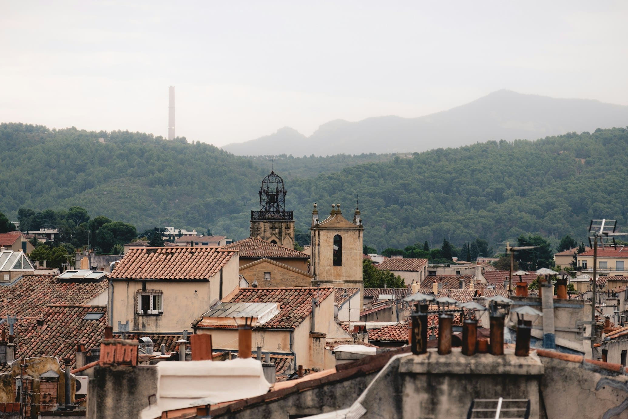 Vista de Aix-en-Provence, com telhados vermelhos, igrejas antigas e colinas verdes ao fundo.