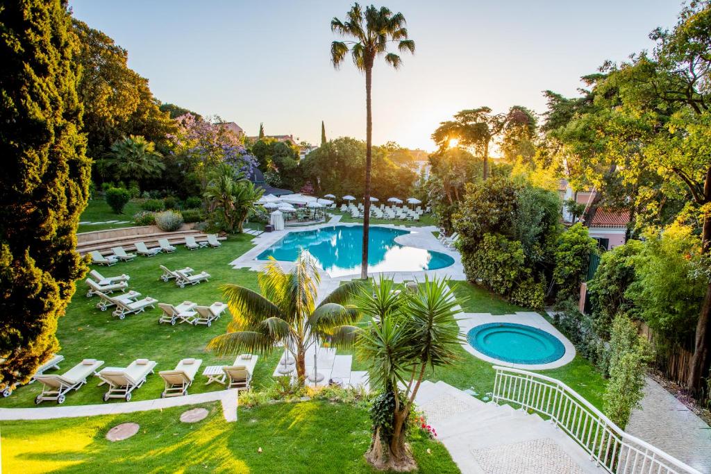 Extenso jardim do Olissippo Lapa Palace com piscina rodeada por espreguiçadeiras e árvores