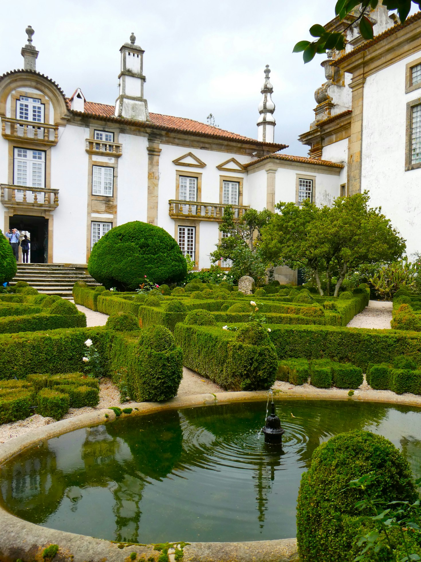Palácio de Mateus, jardim formal com sebes bem cuidadas, uma pequena fonte circular e um edifício histórico ao fundo.