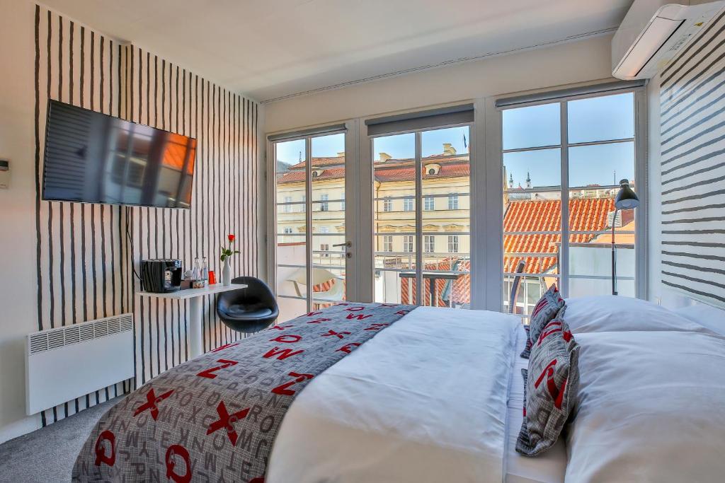 Quarto do LH Vintage Design Hotel Sax, com cama de casal, TV, cadeira e janelas grandes com vista sobre a cidade e os seus telhados vermelhos.
