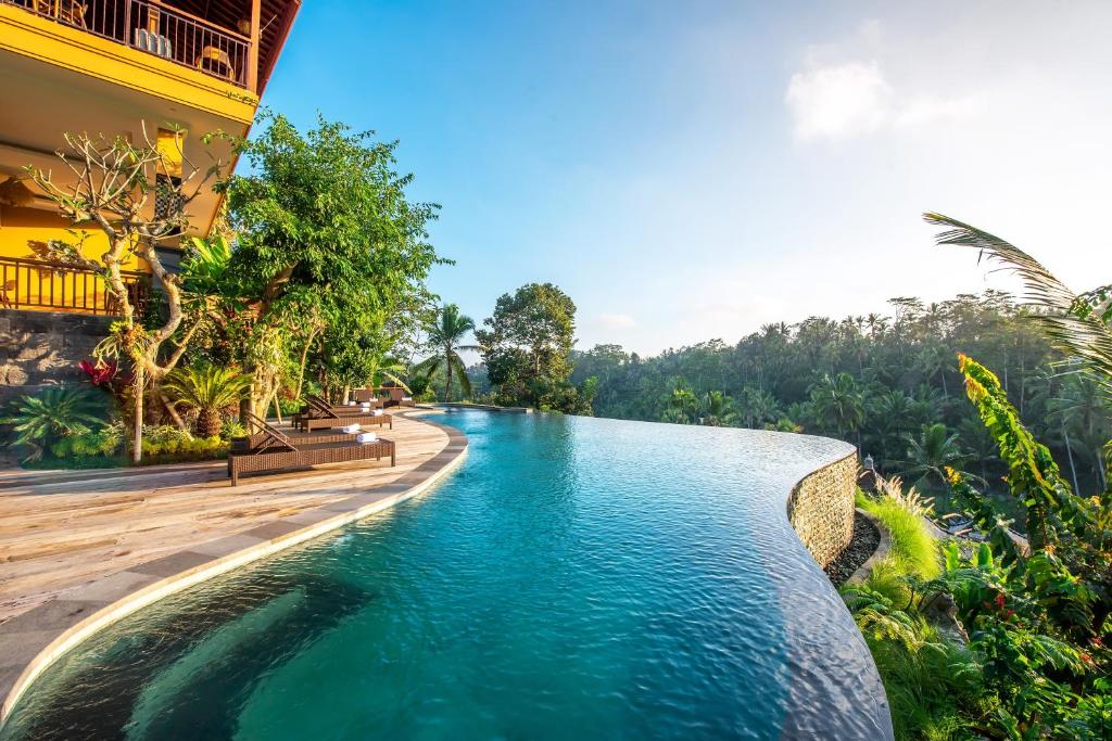 Piscina infinita com vista para uma paisagem verdejante, junto a um edifício amarelo, no GK Bali Resort, em Bali.