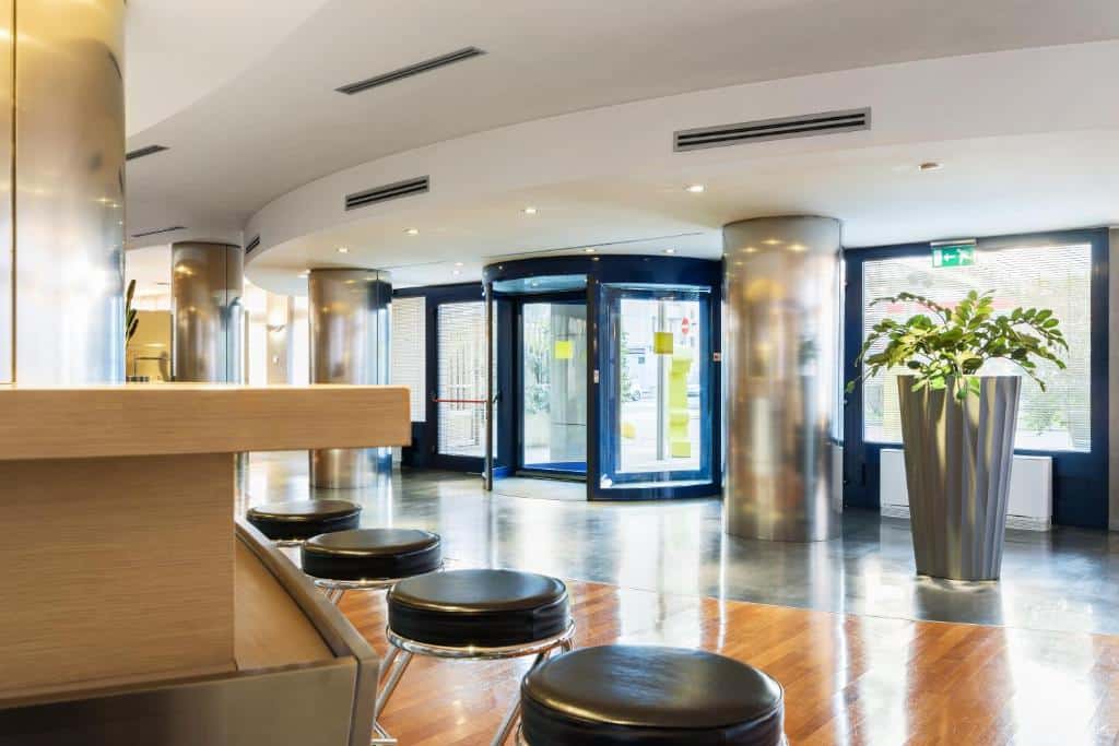 Receção ampla e arejada com porta giratória, balcão e mesas altas no B&B Hotel Milano La Spezia