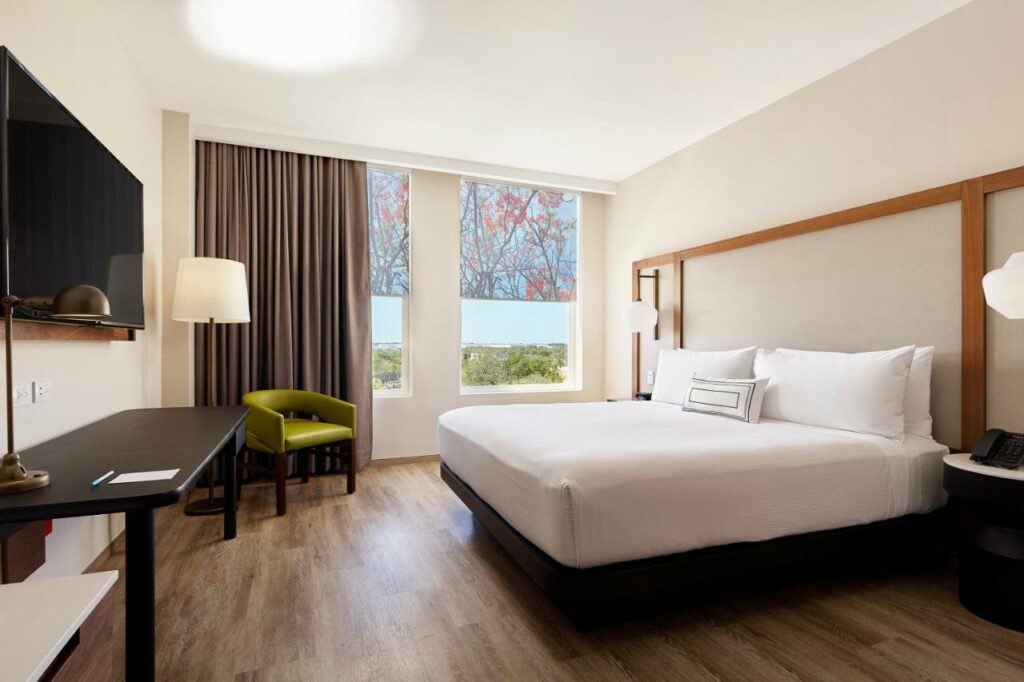 Quarto amplo no Fairfield Inn & Suites by Marriott Cancun Airport com janela com vista para o jardim, cama de casal, poltrona, candeeiro de pé, secretária e televisão